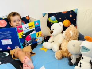 Michele sentado en la cama leyendo un libro a sus peluches